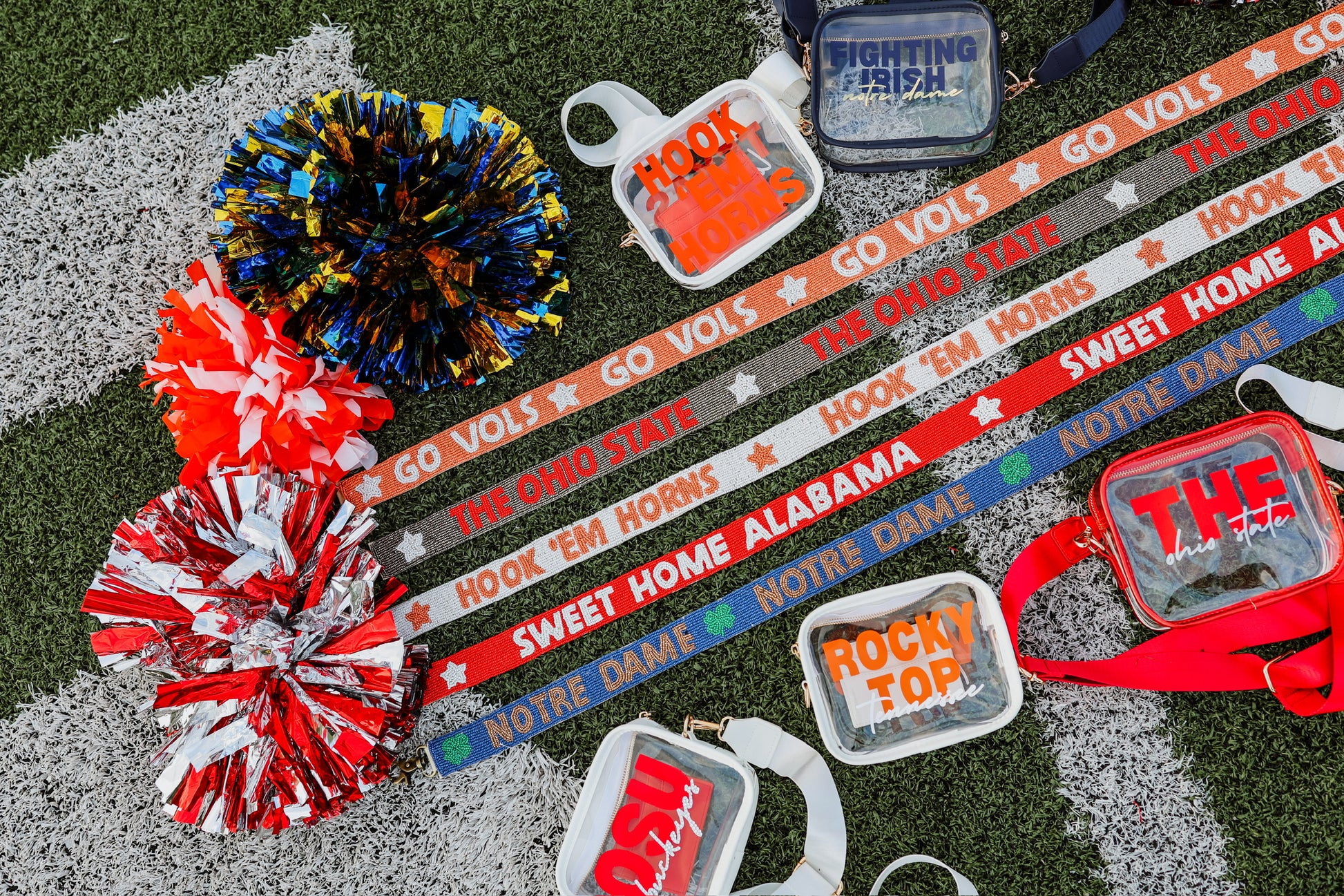 Colorful pom-poms and sports-themed accessories on a grassy surface with cleat stadium purses and beaded purse straps