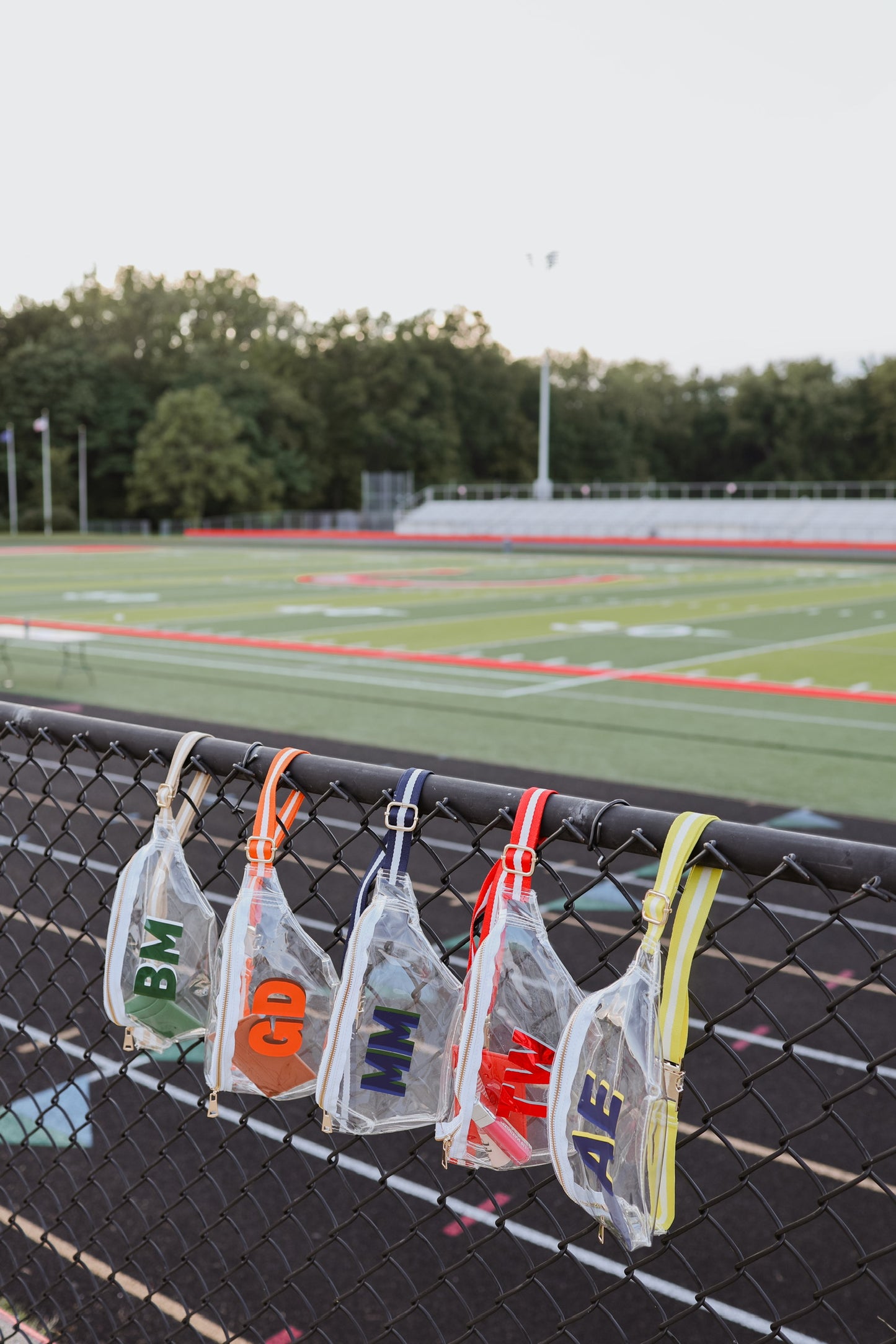 Monogrammed fanny packs hanging on a fence with a sports field in the background