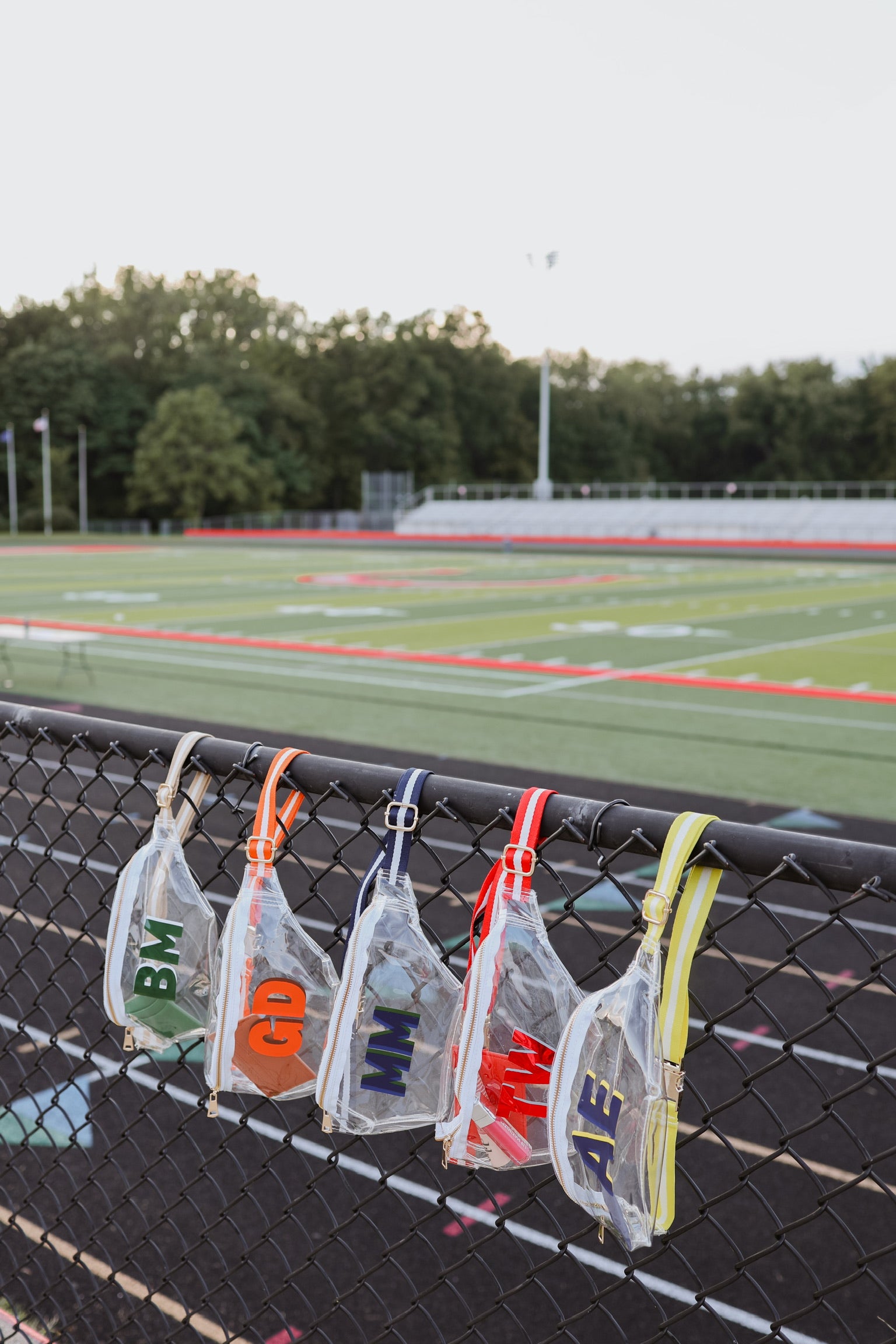 Monogrammed fanny packs hanging on a fence with a sports field in the background