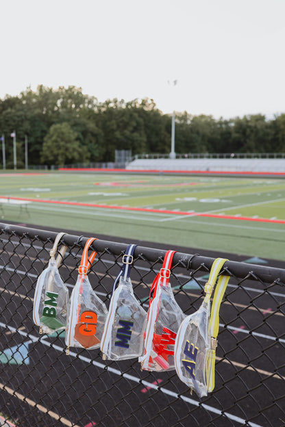 Monogrammed fanny packs hanging on a fence with a sports field in the background