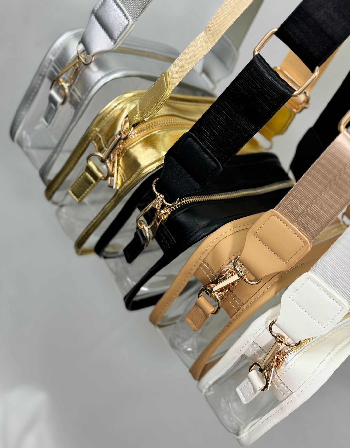 Set of clear bags with gold, black, beige, and white straps on a light gray background