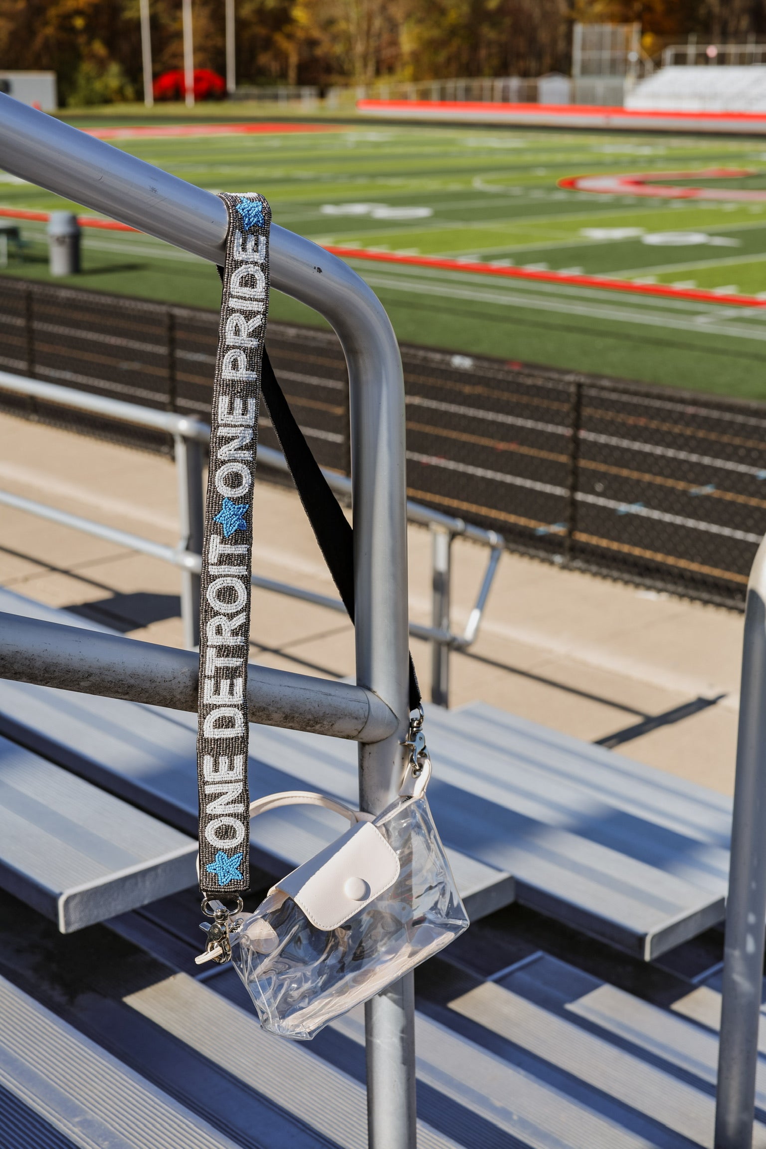 Clear bag with 'One Detroit Pride' strap attached to metal bleachers on a football field.