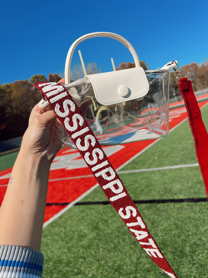 Clear handbag with white leather handle with a red strap displaying 'Mississippi State' on a sports field.